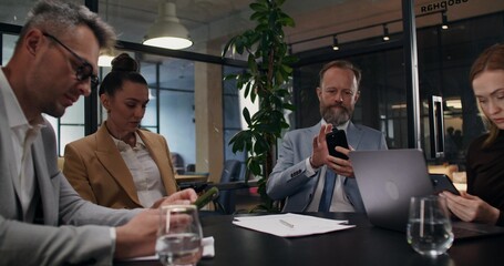 A group of stylish business people use mobile phones while sitting at the same desk in the office
