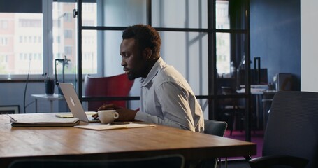 A man works in the office. He uses a laptop with a serious look.