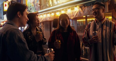 Funny young people spend time together. They drink beer and talk while standing on a city street at night.