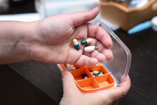 Hands filling a weekly pill organizer with medications, showcasing organized healthcare management