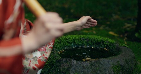 A Japanese woman in a kimono draws water from a stone. Close-up of her hand, unrecognizable person