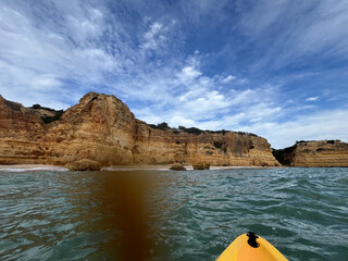 Kayak gliding through serene ocean waters, surrounded by majestic cliffs under a vast sky,...