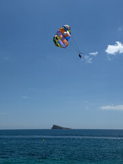 parasailing with Colorful parachute gliding over tranquil blue sea, with a distant rocky island under a bright summer sky, capturing the essence of adventure and escapism in vacation travel
