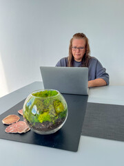 Midlife woman working remotely on a laptop at a stylish table, surrounded by decorative elements,...