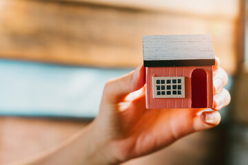 Miniature Wooden House Model Held by Hand with Soft Light in Background for Real Estate Concepts
