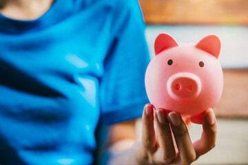 Pink Piggy Bank Held by Person with Blue Shirt in Modern Indoor Background