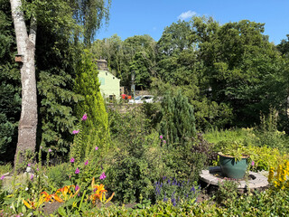 “Beneath a clear blue hush, tall trees and bright blossoms sway in a sunlit garden. Amid the green, a house of jade quietly nestles, half-dreamt through the veil of foliage on, Goit Stock Lane, Harden