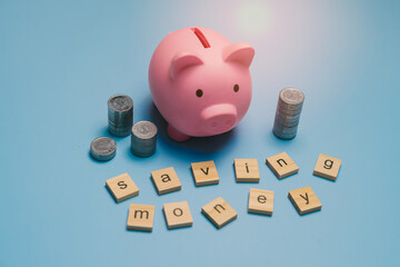 Saving money concept. Creative Concept of Saving Money with Pink Piggy Bank and Coins on Blue...