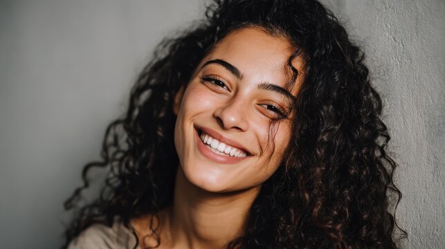 Close up face of young woman with beautiful smile isolated on grey wall with copy space. Successful multiethnic girl. Latin woman looking at camera against gray wall with a big whitening teeth smile.