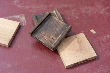Three wooden blocks rest on a reddish surface two are dark brown with edge grooves suggesting assembly use
