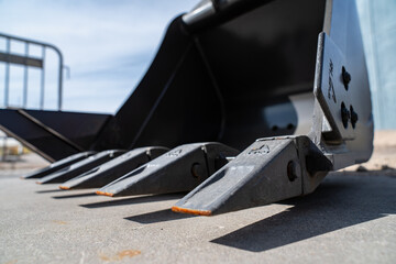 heavy duty excavator bucket teeth attachment on construction machinery resting on concrete ground...