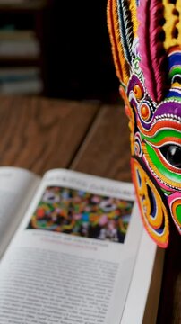 Colorful wooden mask resting on open book about chhau dance