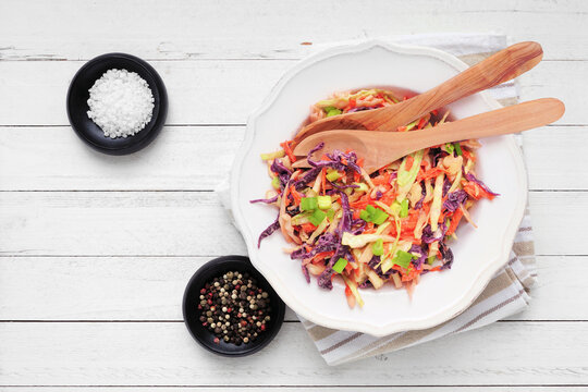 Classic coleslaw salad with colorful cabbage, carrots and mayonnaise. Top down table scene on a white wood background.