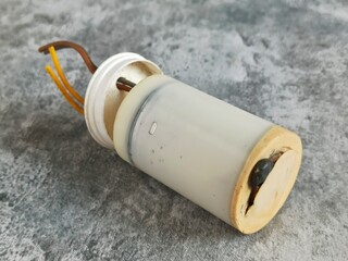 Close-up of an old electrical capacitor with exposed wires and worn casing, placed on a textured...