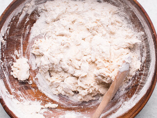 Overhead view of bread dough being mixed in a wooden bowl, top view of homemade bread dough in a...
