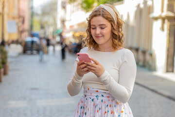 Redhead young woman in long dress using smartphone typing texting social media messages e-mail...