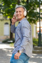 Rear view of happy man tourist in wireless headphones choosing, listening favorite energetic disco...