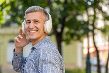 Rear view of happy man tourist in wireless headphones choosing, listening favorite energetic disco...