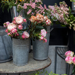 Various pink flowers in metal buckets are displayed on a metal table.