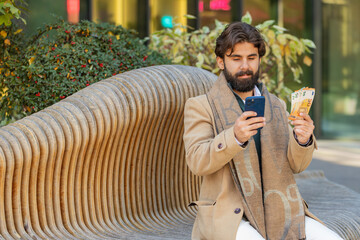 Happy rich Indian businessman tourist using smartphone and counting money euro cash banknotes...