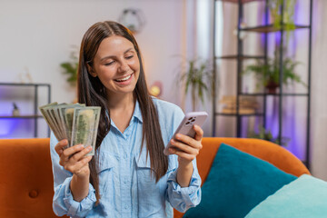 Smiling happy rich Caucasian young woman counting money cash, use smartphone calculate domestic...
