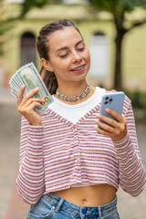 Happy rich young woman with braces on teeth counting money dollar cash, use smartphone calculator...