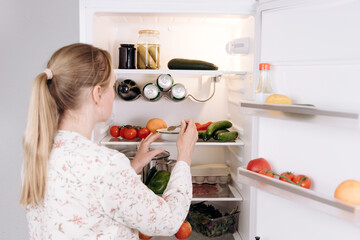 Woman  long blonde hair, wearing floral blouse, is organizing fresh vegetables and fruits in a...