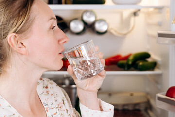 Woman holding glass of cold water, contemplating potential dangers of drinking cold beverages from...