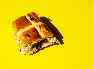 Fine cross bun on warm yellow background, hard lighting, Tasty bakery product. Popular traditional desert.