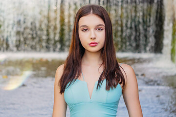 Stunning young girl in blue fashion dress posing in water with waterfall in the background. Model...
