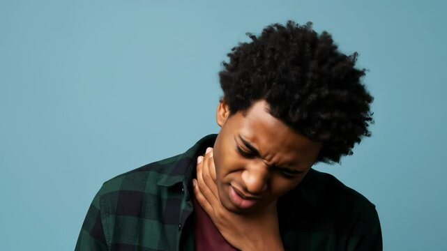 Sore throat suffering: Black man in his 20s clutches his throat with a painful expression against a light blue background.