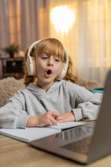 Young girl wearing wireless headphones listening to English audio lesson at home repeating new...