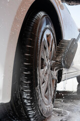 Car wash worker cleaning wheel and tire with brush and soap