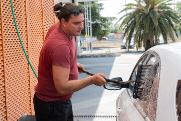 Man washing car window with brush and soap at self service car wash