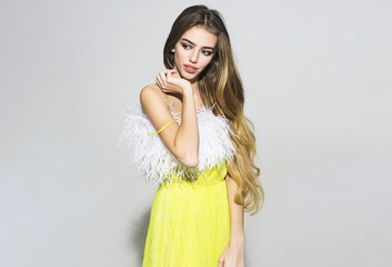 Beautiful young woman in stylish yellow dress with feathers looking away. Female model with perfect...
