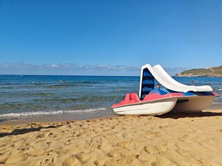 A vibrant beach scene in Annaba, Algeria, features a colorful pedal boat on golden sand with clear...