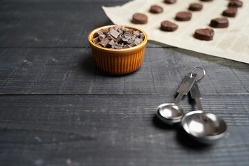 Front view of cookie dough cut on baking paper with chocolate chips in a brown bowl and spoon on black wooden background