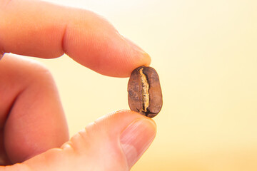 hand holds a single roasted coffee bean, split to reveal its core, against a warm beige backdrop....