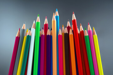 Fototapeta premium A collection of sharpened colored pencils in bright shades, organized in a visually appealing row against a minimalist gray background. Great for art and stationery concepts.