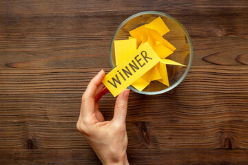 Hand is holding raffle ticket winner near glass jar, top view. Luck and lottery concept