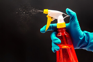 A gloved hand activates a red spray bottle with a yellow nozzle, releasing a fine mist on a black...
