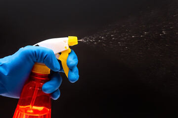 Naklejka premium A gloved hand activates a red spray bottle with a yellow nozzle, releasing a fine mist on a black backdrop, perfect for cleaning product ads or sanitation themes.