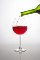 Close-up of a green wine bottle filling a crystal wine glass with deep red wine, showcasing bubbles and flow. Minimalist white backdrop enhances the elegance, great for alcohol brands