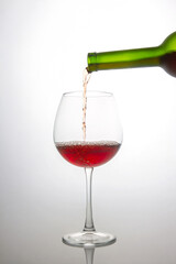 a green wine bottle filling a crystal wine glass with deep red wine, showcasing bubbles and flow. Minimalist white backdrop enhances the elegance