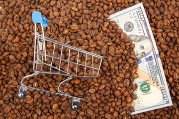 miniature shopping cart placed on roasted coffee beans alongside US dollar bills, representing the...