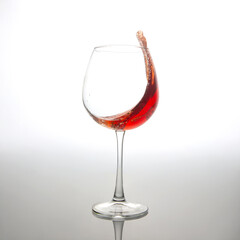 A dramatic splash of red wine captured mid-air, swirling inside a clear wine glass against a soft white background. Perfect for beverage ads, wine culture, or dynamic drink photography