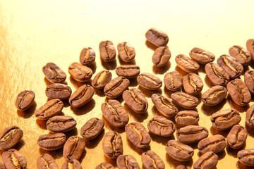 A collection of roasted coffee beans shaped into an oval on a shiny gold background, showcasing...