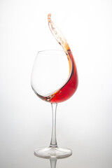 A dramatic splash of red wine captured mid-air, swirling inside a clear wine glass against a soft white background. Perfect for beverage ads, wine culture, or dynamic drink photography