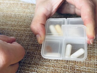 The weekly transparent pill box is designed for convenient and efficient daily storage of dietary supplements and pills. A woman's hand holds a pillbox above the table.