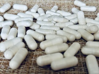 Numerous white capsules scattered over the textured surface create an artistic effect. A close-up of various white capsules for the treatment of human health is shown.
